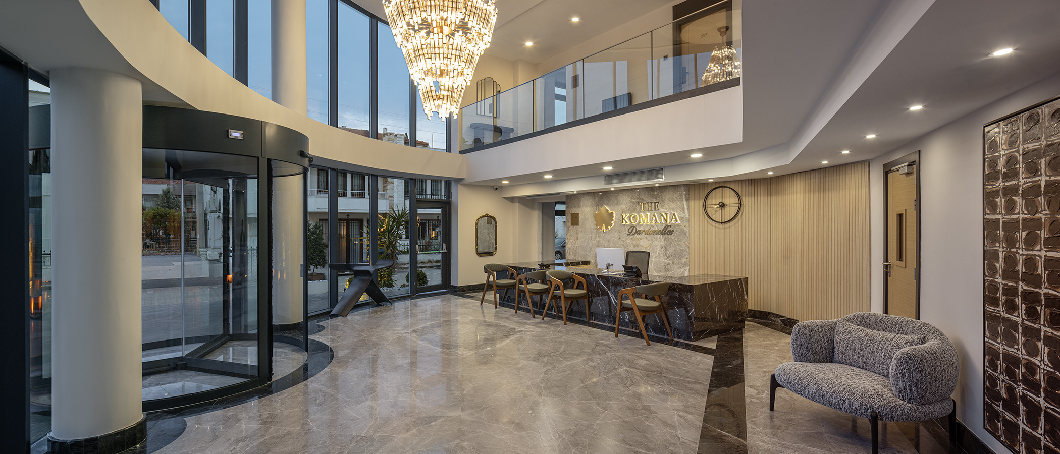 Çift kat yüksekliğinde cam cepheli otel lobisi, avize ve mermer zemin